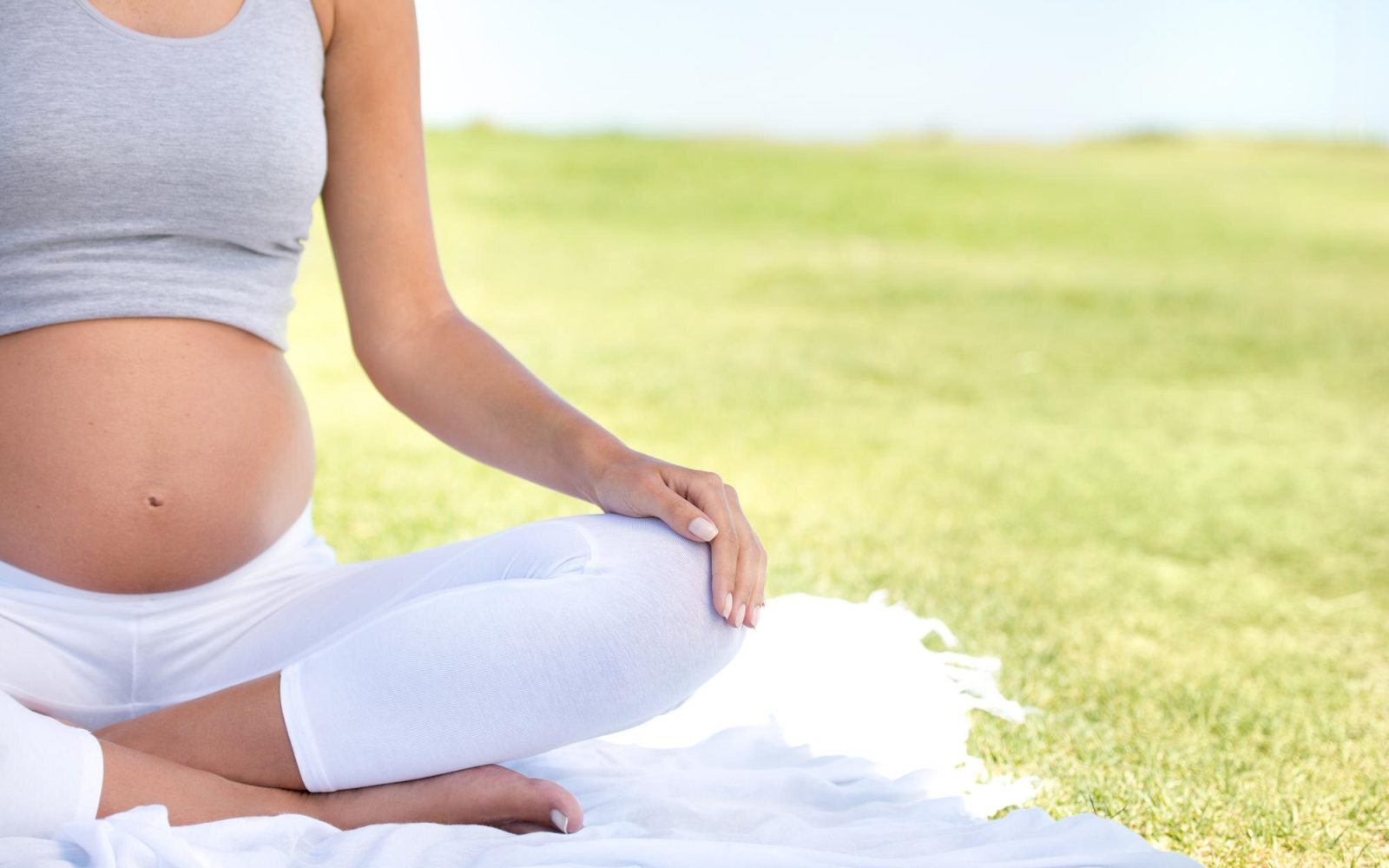 Mujer embarazada sentada con la mano sobre el vientre, en actitud meditativa